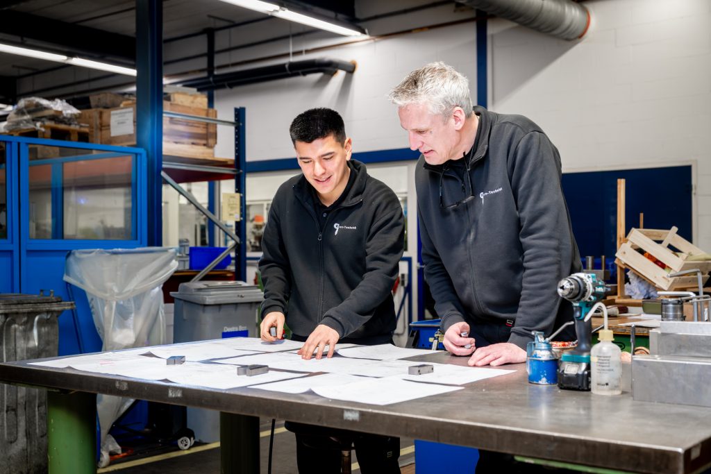 Twee mannen bekijken plannen in werkplaats.