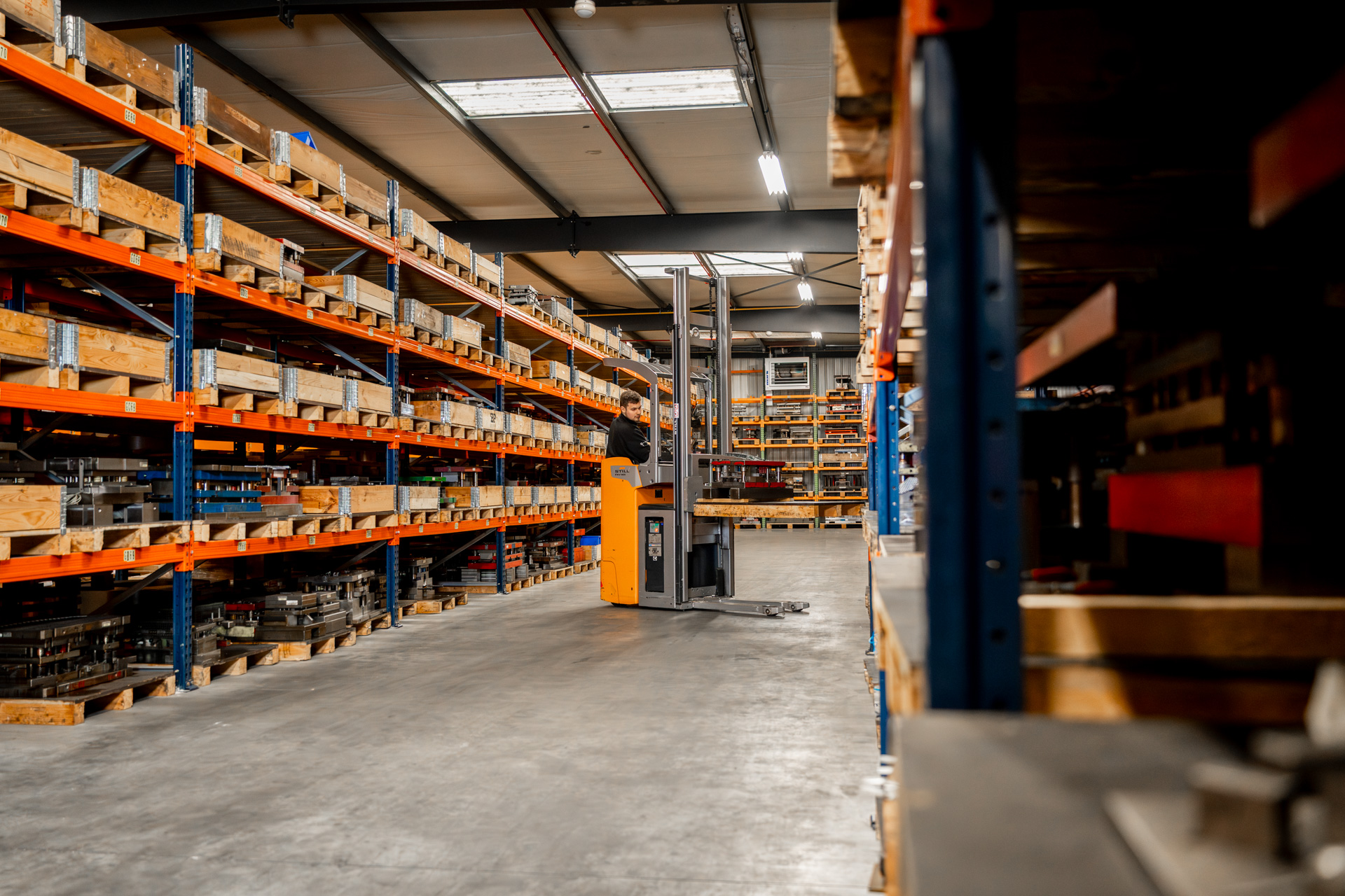 Magazijn met heftruck en planken vol materialen.